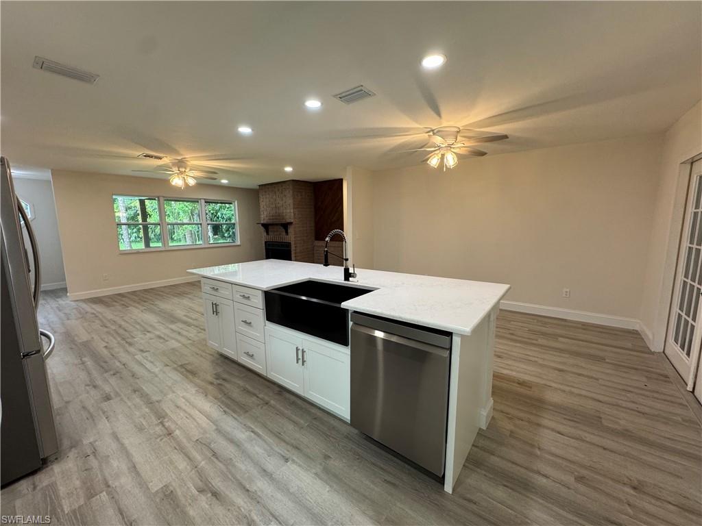 Kitchen featuring a ceiling fan, white cabinetry, recessed lighting, stainless steel appliances, and a center island with sink