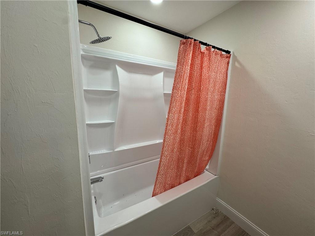 Full bath with a textured wall, shower / tub combo with curtain, and wood finished floors