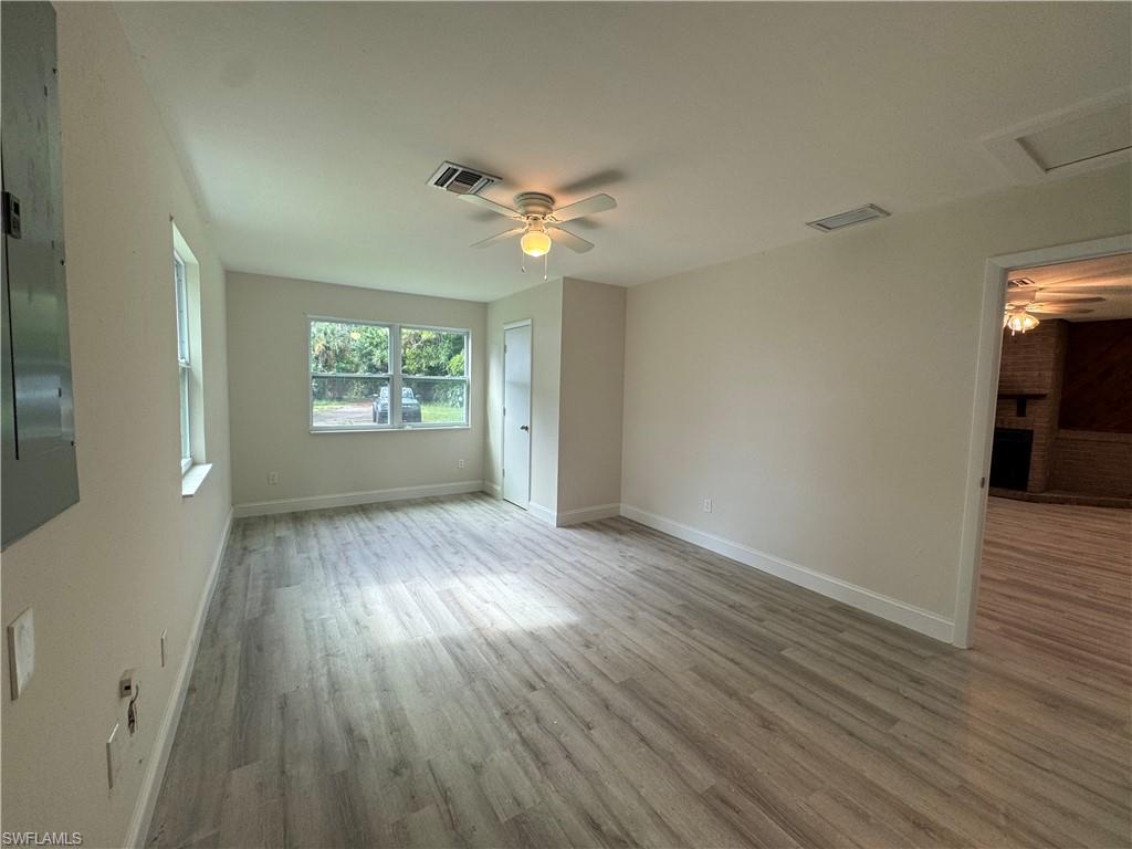Unfurnished bedroom with light wood-type flooring, a brick fireplace, a ceiling fan, and attic access