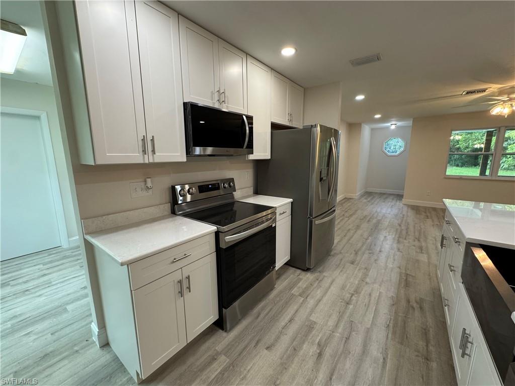 Kitchen with stainless steel appliances, white cabinets, light stone countertops, light wood-style floors, and recessed lighting