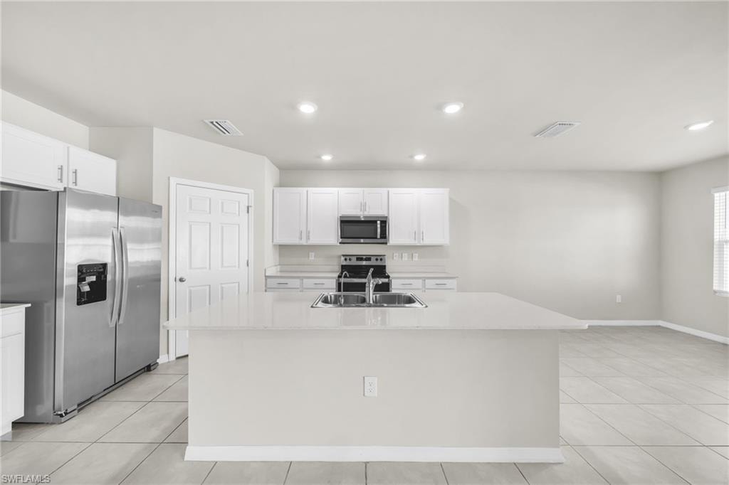 Kitchen featuring stainless steel appliances, an island with sink, white cabinets, light tile patterned floors, and recessed lighting