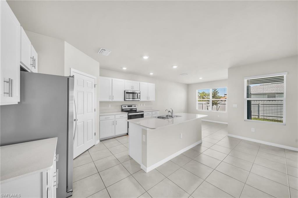 Kitchen with recessed lighting, appliances with stainless steel finishes, an island with sink, light tile patterned flooring, and white cabinetry