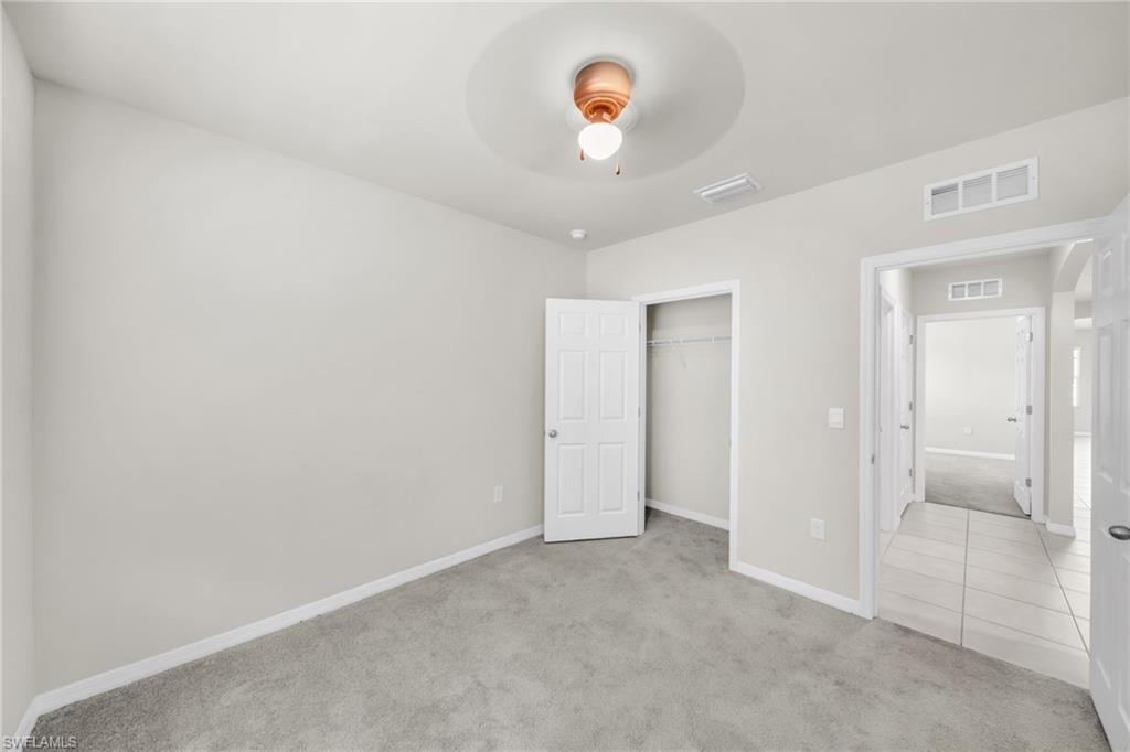 Unfurnished bedroom with light carpet, ceiling fan, a closet, and light tile patterned floors