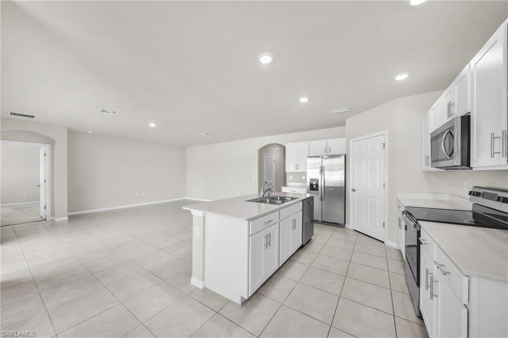 Kitchen with arched walkways, stainless steel appliances, white cabinets, recessed lighting, and an island with sink