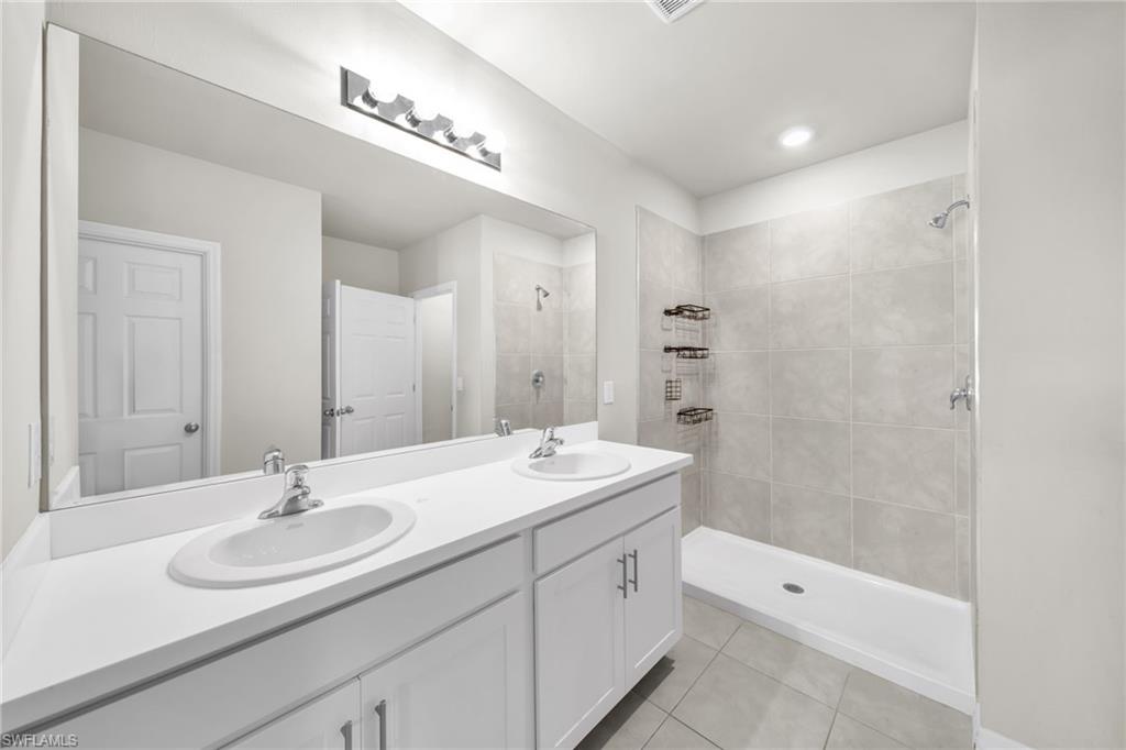 Bathroom with light tile patterned flooring, a stall shower, and double vanity