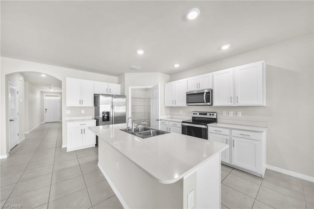 Kitchen featuring white cabinets, stainless steel appliances, arched walkways, a kitchen island with sink, and recessed lighting