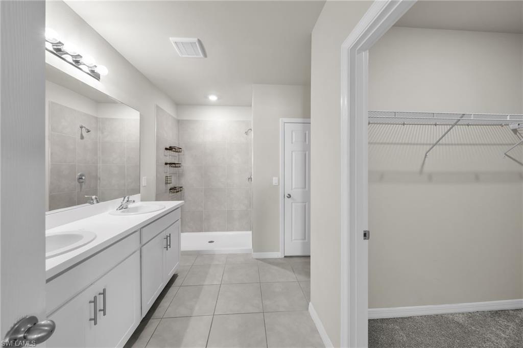 Full bathroom featuring a stall shower, light tile patterned floors, double vanity, and a walk in closet
