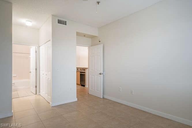 Unfurnished bedroom with ensuite bathroom and light tile floors