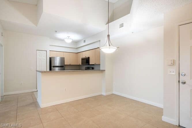 Kitchen featuring decorative light fixtures, light brown cabinets, kitchen peninsula, appliances with stainless steel finishes, and light tile floors