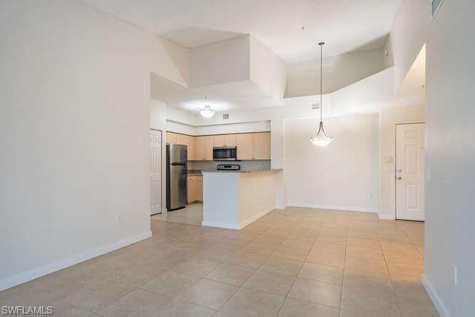 Kitchen with appliances with stainless steel finishes, a high ceiling, pendant lighting, light tile flooring, and light brown cabinets