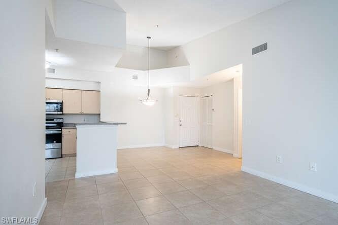 Kitchen with hanging light fixtures, a high ceiling, range, and light tile flooring