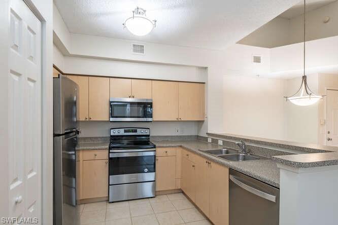 Kitchen with stainless steel appliances, light tile floors, decorative light fixtures, sink, and light brown cabinetry