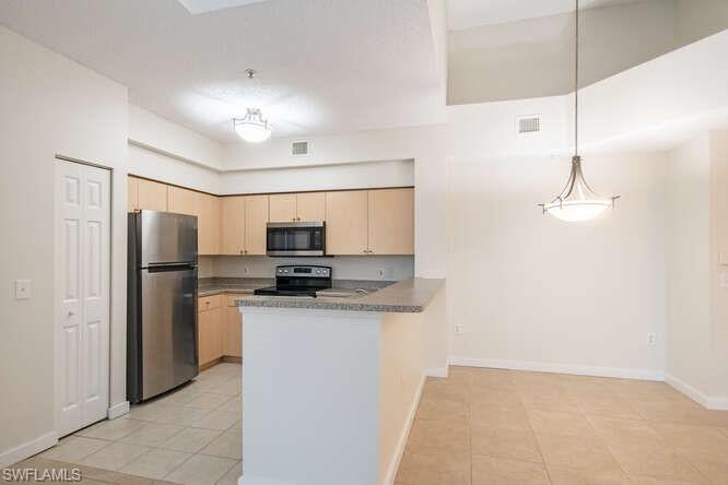 Kitchen with light brown cabinets, appliances with stainless steel finishes, light tile flooring, and kitchen peninsula