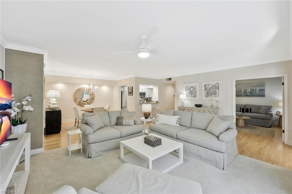 Living room featuring ceiling fan, wood finished floors, a chandelier, and ornamental molding