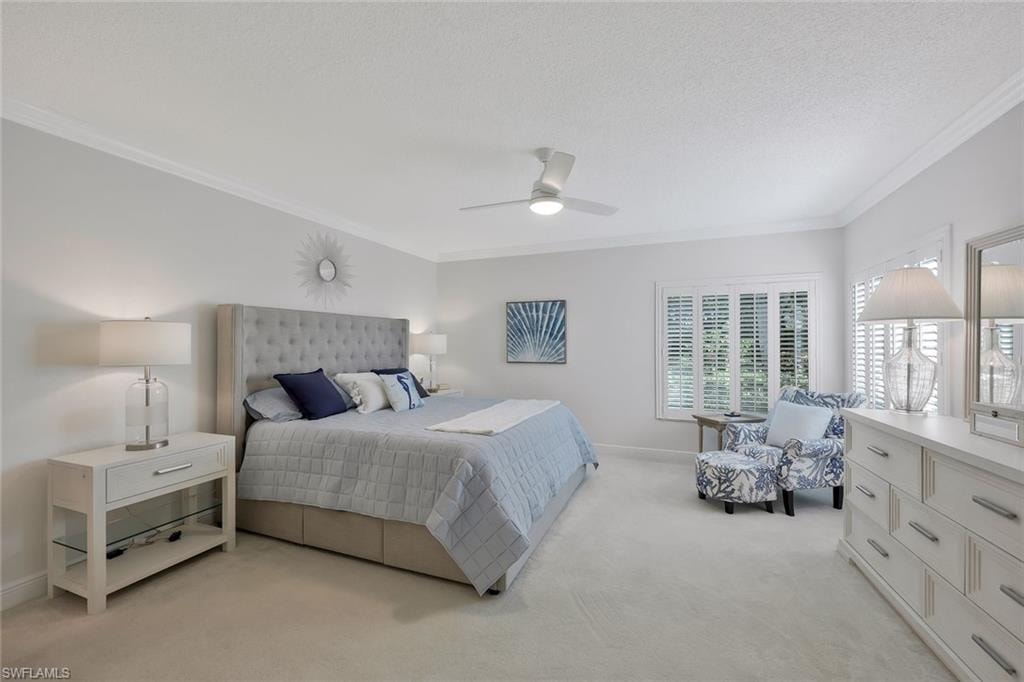 Bedroom with ornamental molding, light carpet, a ceiling fan, and a textured ceiling