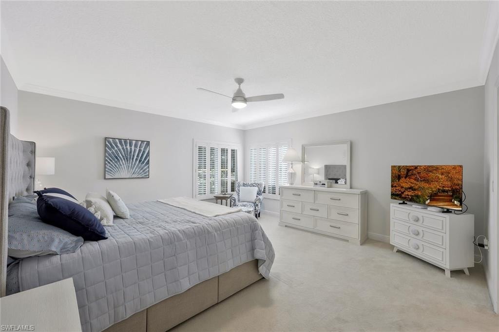 Bedroom featuring light colored carpet, ornamental molding, and ceiling fan