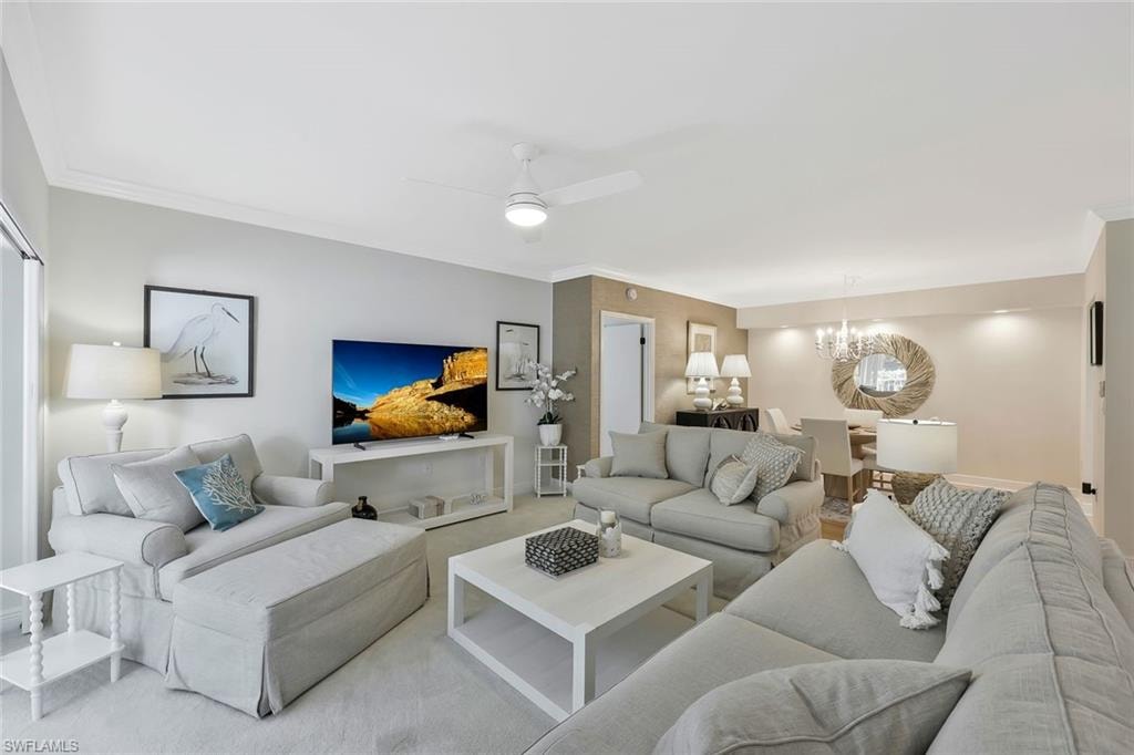 Living room featuring a ceiling fan, a chandelier, and ornamental molding