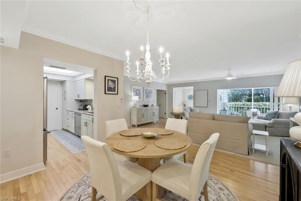 Dining area featuring light wood finished floors, a chandelier, crown molding, and a ceiling fan