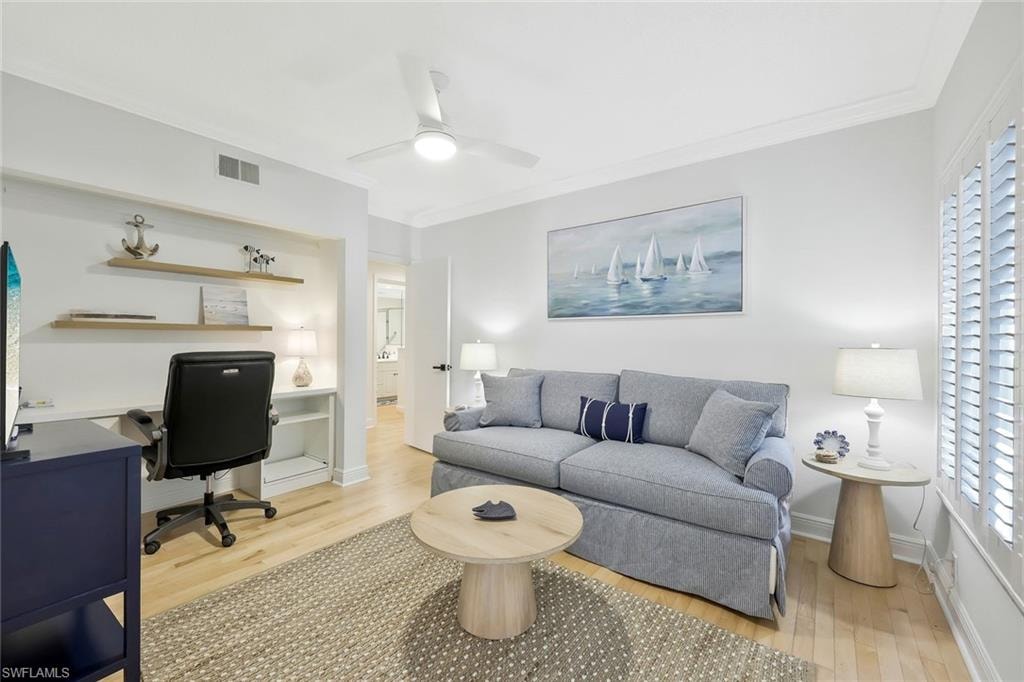 Living room with an office area, light wood finished floors, ornamental molding, and a ceiling fan