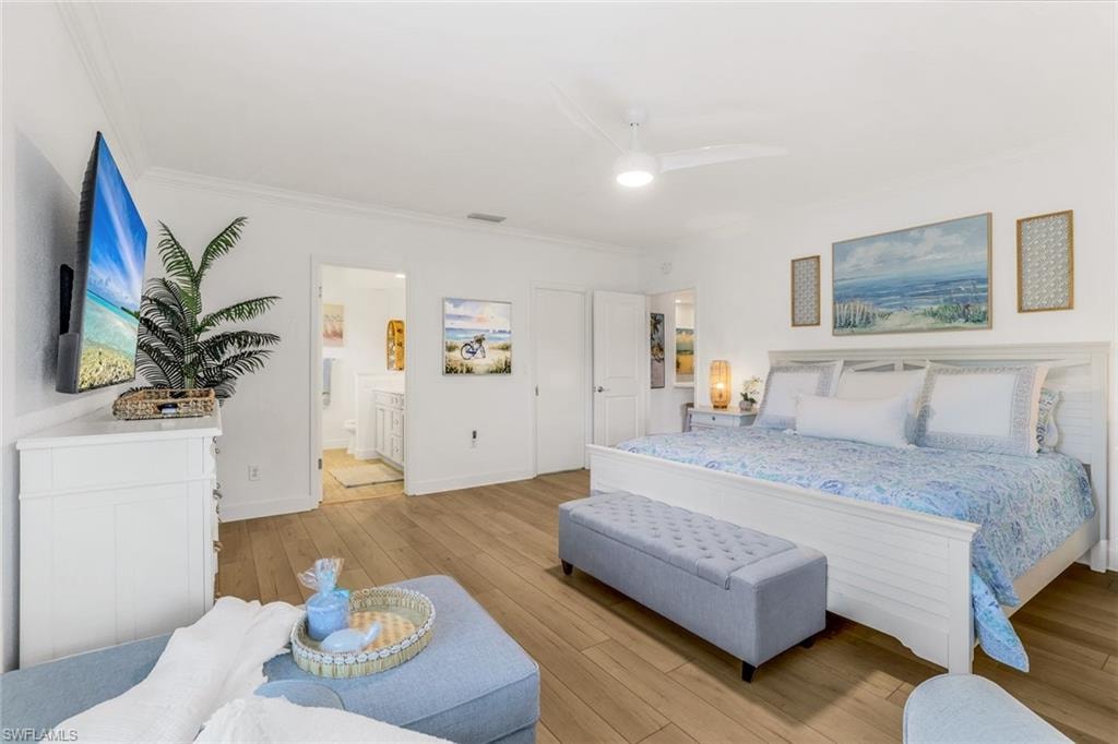 Primary suite with a king size bed, light vinyl plank floors, ceiling fan, and ornamental molding