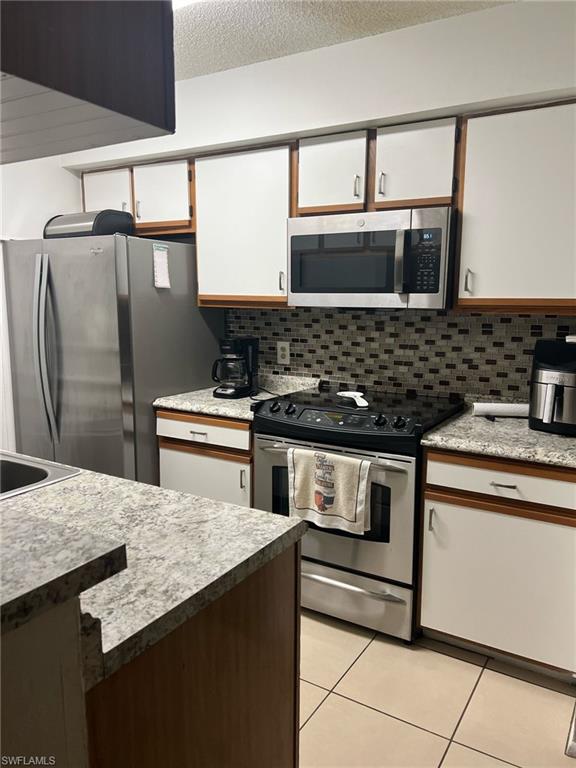 Kitchen featuring appliances with stainless steel finishes, light tile patterned flooring, backsplash, white cabinetry, and a textured ceiling