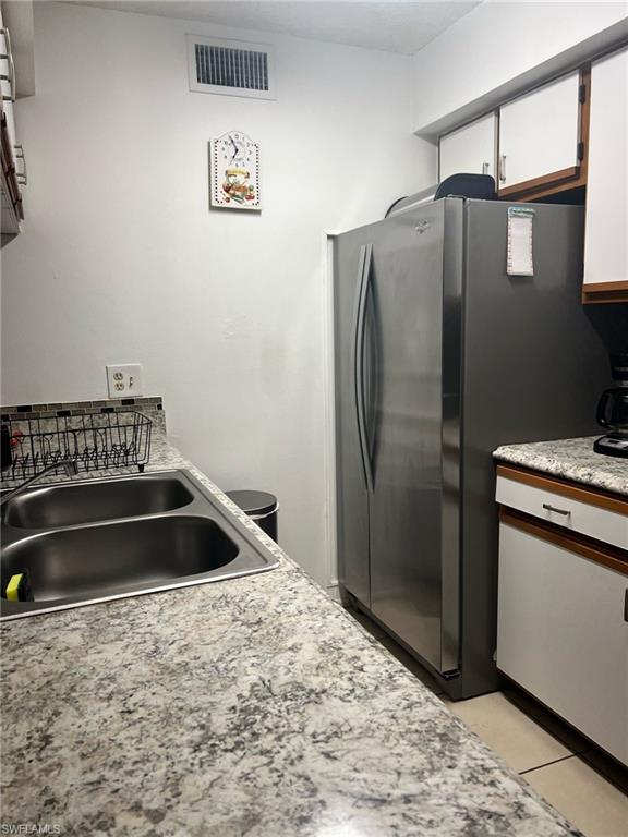 Kitchen featuring freestanding refrigerator, light countertops, white cabinets, and light tile patterned floors