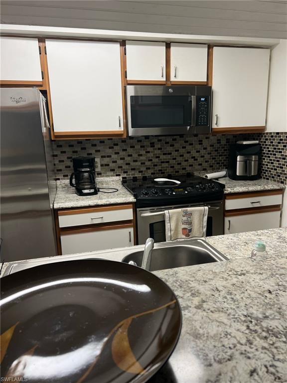 Kitchen with electric range, freestanding refrigerator, decorative backsplash, and white cabinets