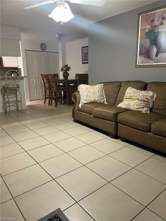 Living area with a ceiling fan, light tile patterned flooring, and a textured ceiling