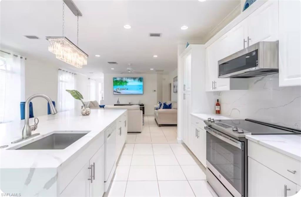 Kitchen with appliances with stainless steel finishes, white cabinetry, hanging light fixtures, open floor plan, and recessed lighting
