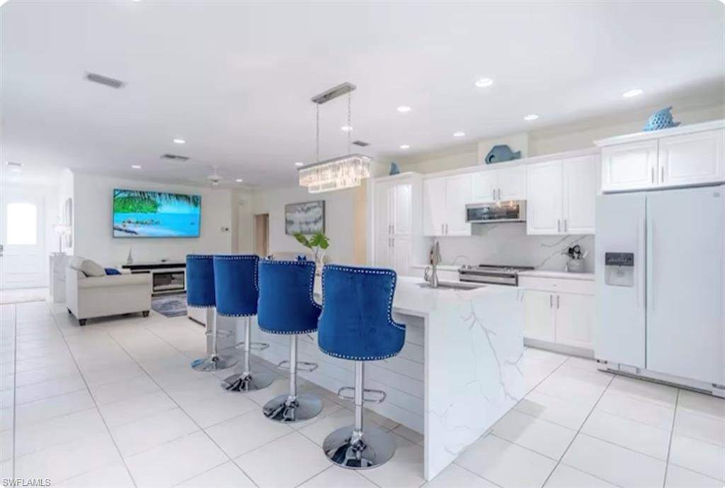 Kitchen with stainless steel appliances, white cabinetry, light tile patterned floors, hanging light fixtures, and a breakfast bar