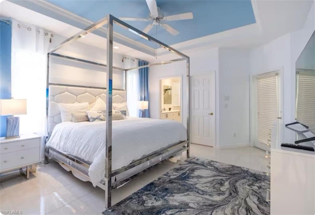 Bedroom with light tile patterned flooring, a tray ceiling, ceiling fan, and ensuite bath