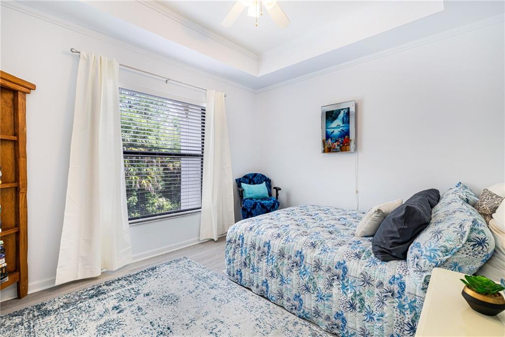 Bedroom featuring a raised ceiling, crown molding, wood finished floors, and a ceiling fan