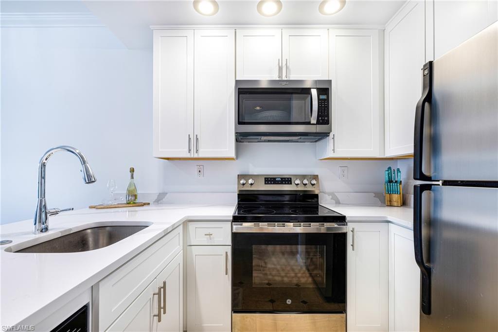 Kitchen featuring stainless steel appliances, white cabinets, and light stone counters