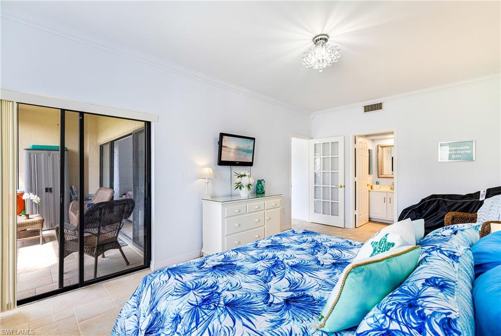 Bedroom featuring crown molding, ensuite bath, access to exterior, light tile patterned floors, and a chandelier