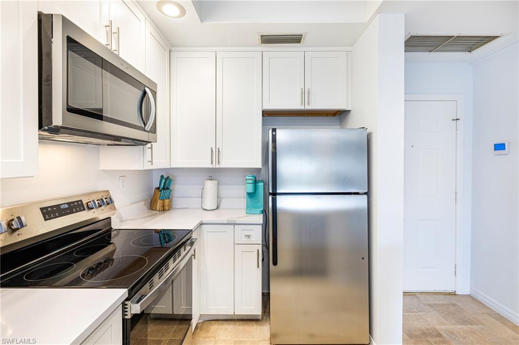 Kitchen featuring stainless steel appliances, white cabinetry, and light stone countertops