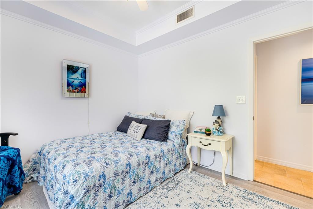 Bedroom with wood finished floors, crown molding, a tray ceiling, and a ceiling fan