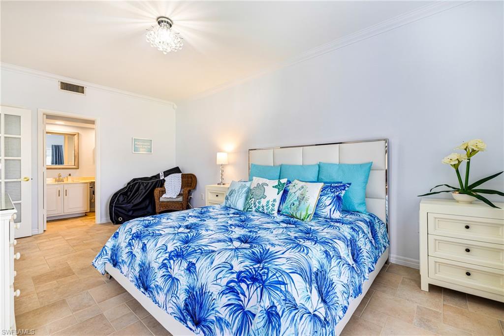 Bedroom with ornamental molding, connected bathroom, a chandelier, and light stone finish flooring