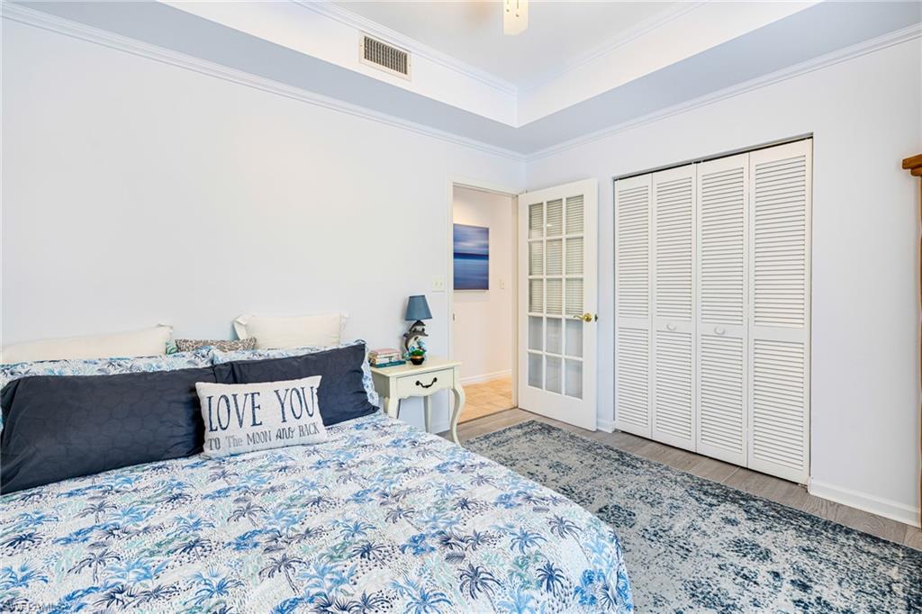 Bedroom with wood finished floors, a raised ceiling, ornamental molding, and a closet