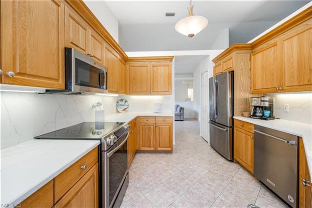 Kitchen featuring appliances with stainless steel finishes, backsplash, and decorative light fixtures