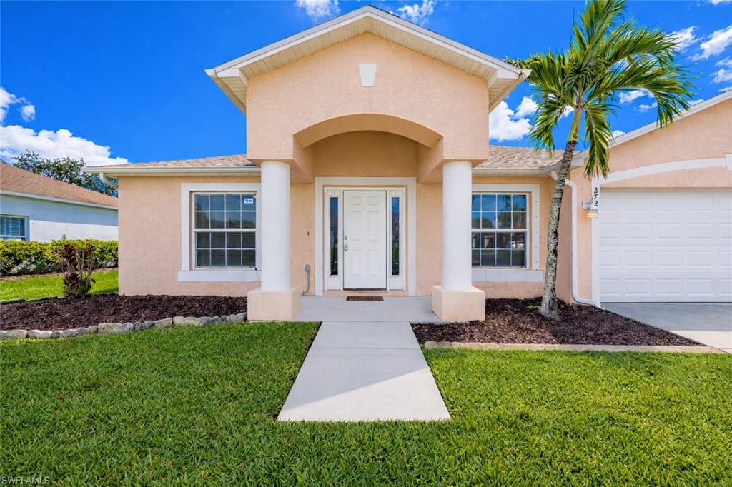 Doorway to property featuring stucco siding, a lawn, an attached garage, and driveway