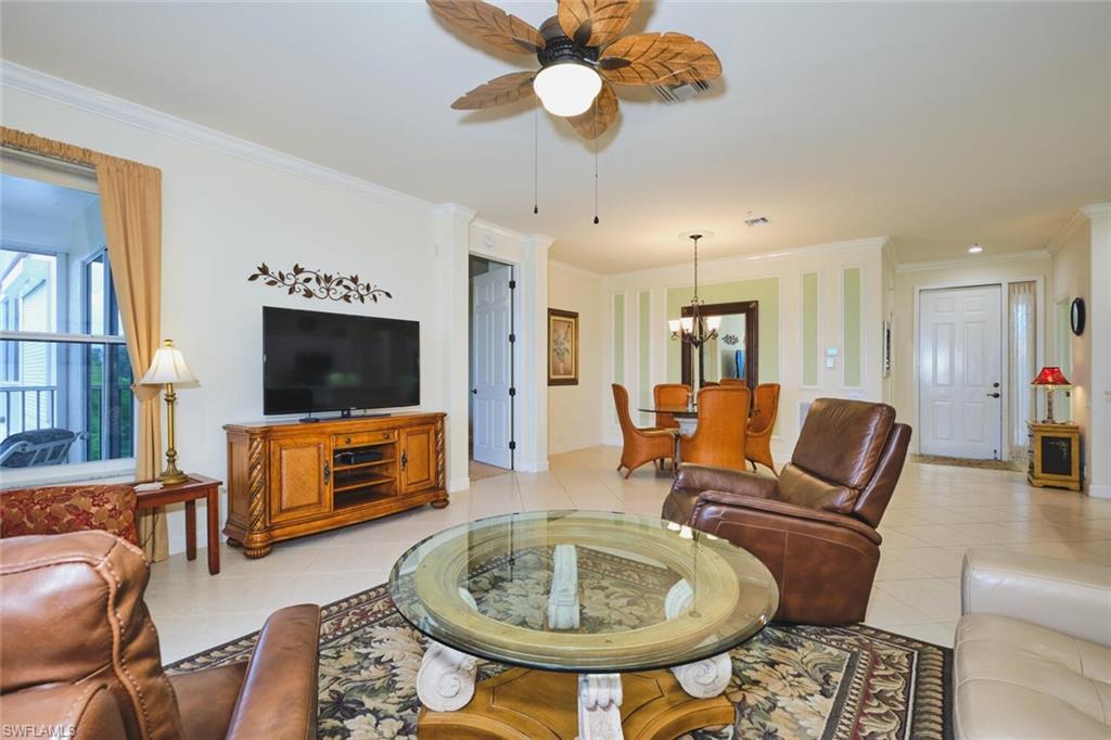 Living room with ornamental molding, light tile patterned floors, a ceiling fan, and a chandelier