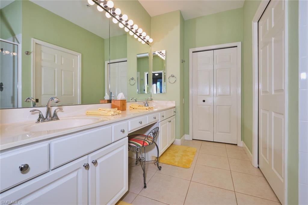 Bathroom featuring a closet, double vanity, light tile patterned flooring, and a stall shower