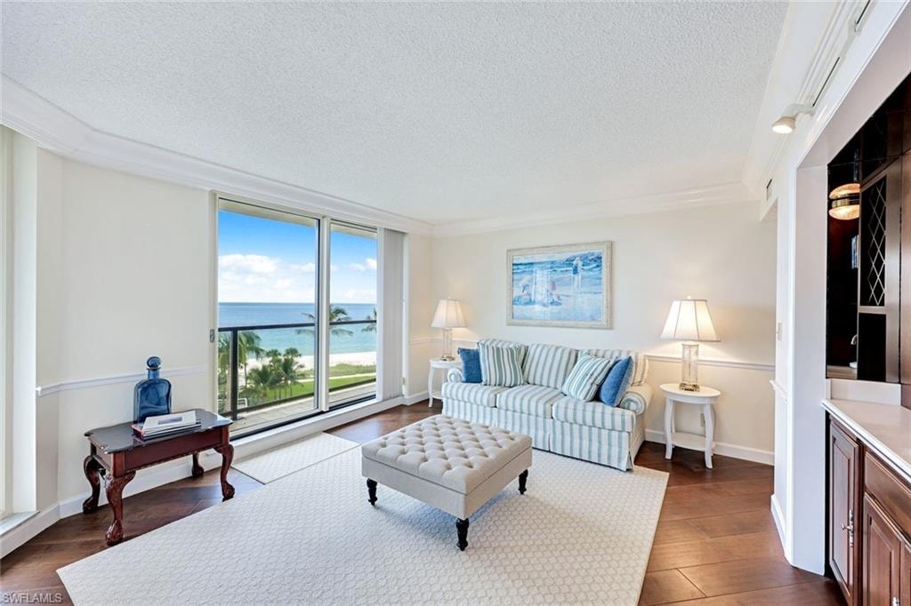 Living room featuring a textured ceiling, a water view, dark wood-style floors, and crown molding