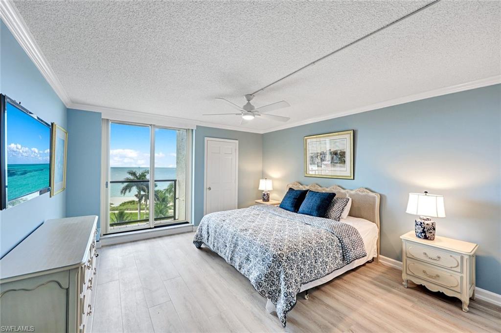 Bedroom featuring ornamental molding, a textured ceiling, a water view, light wood-style floors, and a ceiling fan
