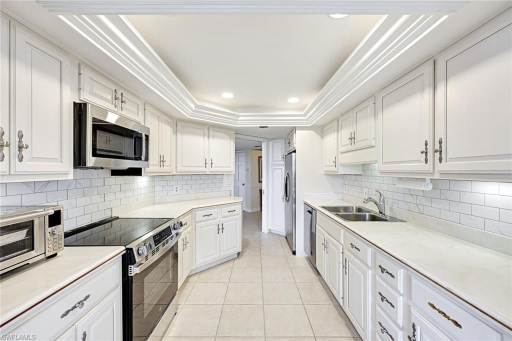 Kitchen with appliances with stainless steel finishes, white cabinets, light countertops, recessed lighting, and ornamental molding