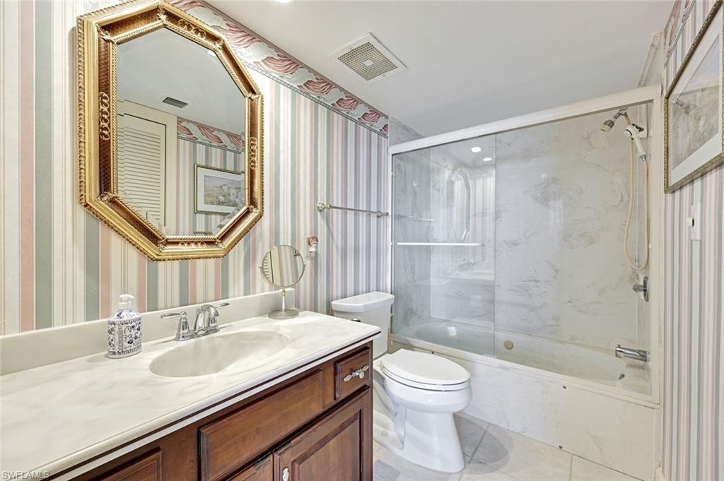 Full bathroom with combined bath / shower with glass door, wallpapered walls, vanity, and light tile patterned flooring