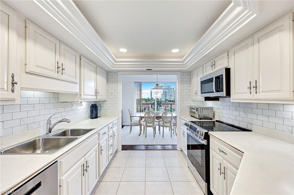 Kitchen with a tray ceiling, stainless steel appliances, light countertops, light tile patterned flooring, and recessed lighting
