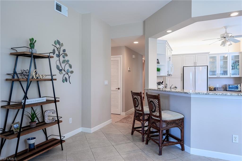 Kitchen with white refrigerator, a breakfast bar area, white cabinets, light tile patterned floors, and light stone countertops