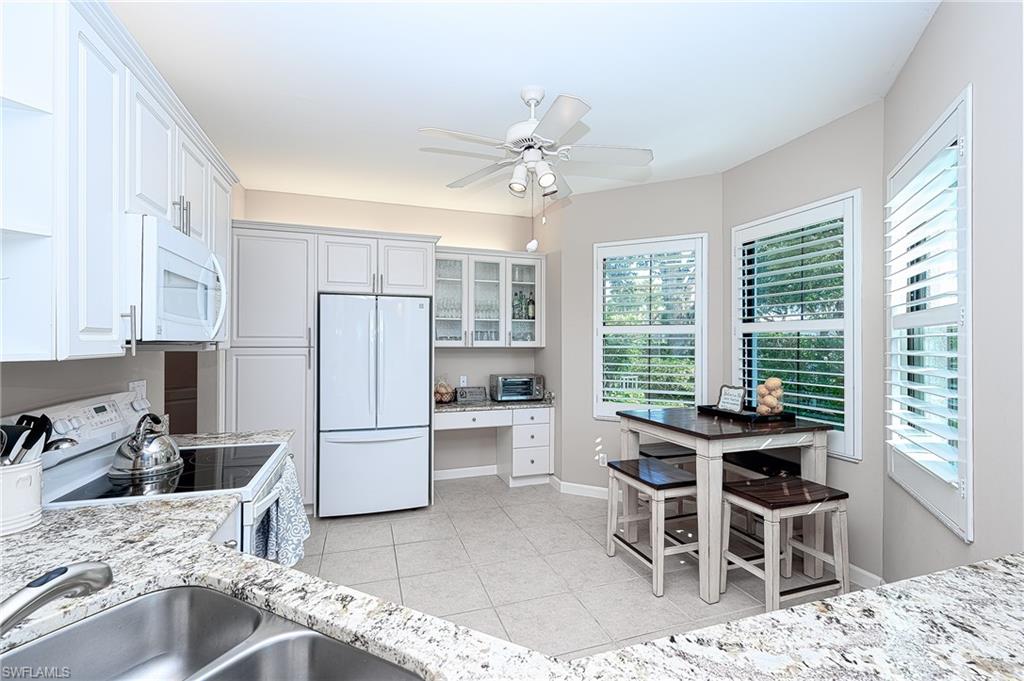 Kitchen featuring ceiling fan, white cabinets, light stone counters, sink, and white appliances