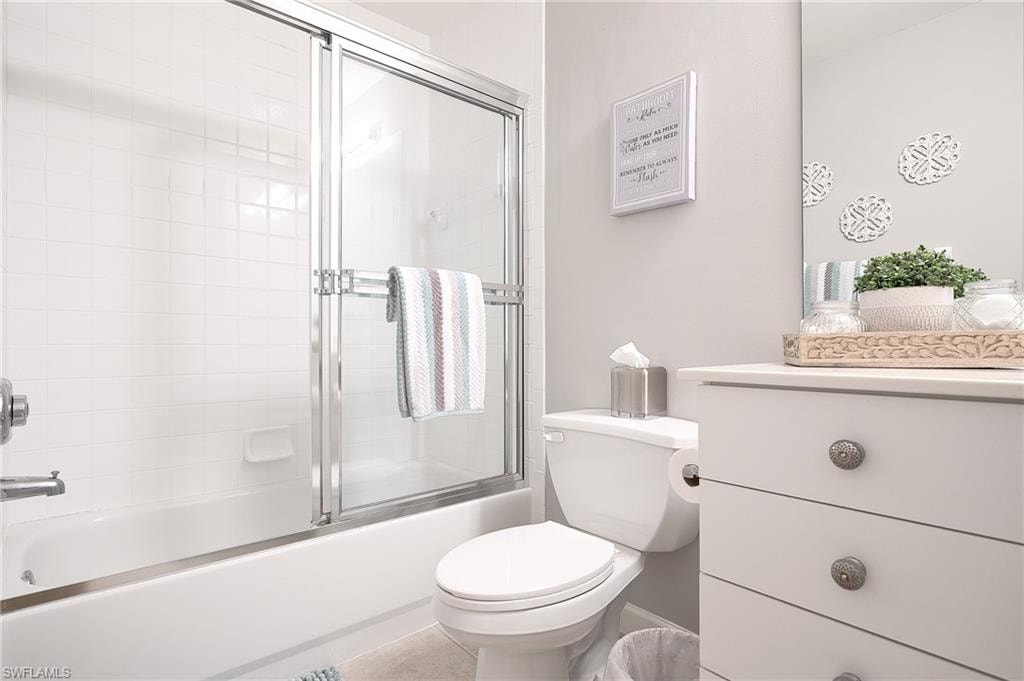 Full bathroom featuring tile patterned flooring, bath / shower combo with glass door, vanity, and toilet